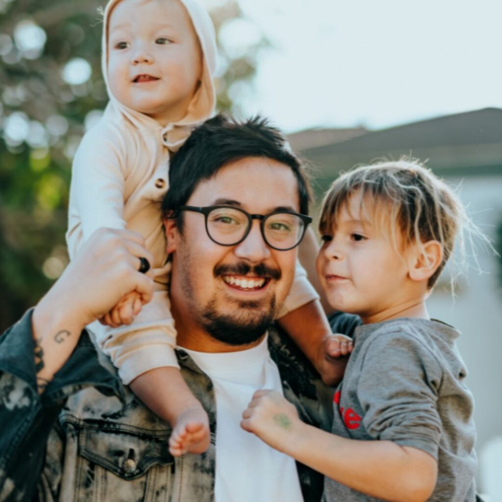 Photo of a father with two children happily standing outside a house